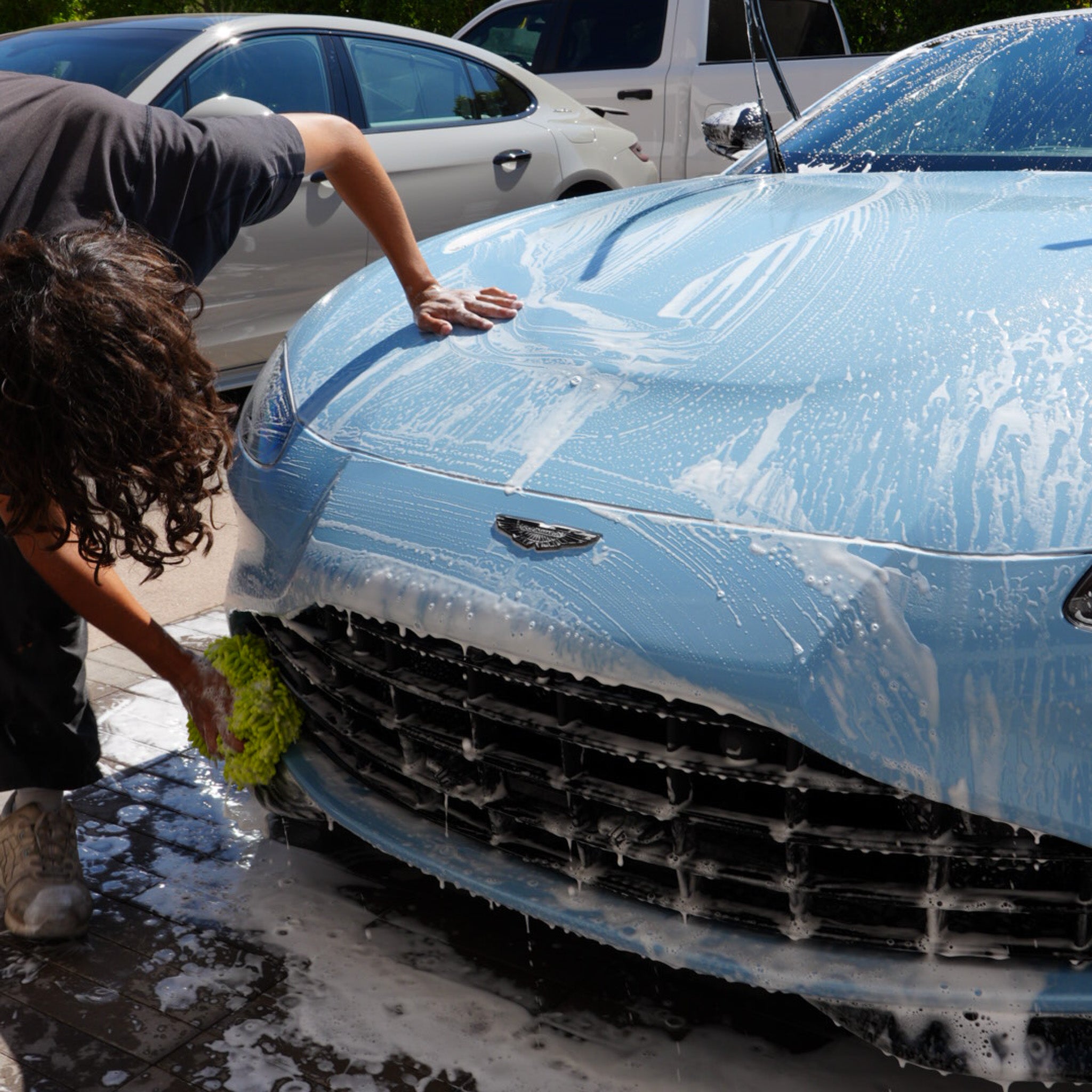 Pure Power Detailing contractor performing a hand foam wash on a light blue Aston Martin, carefully cleaning the front grille and hood during a mobile detail service in Phoenix, Arizona