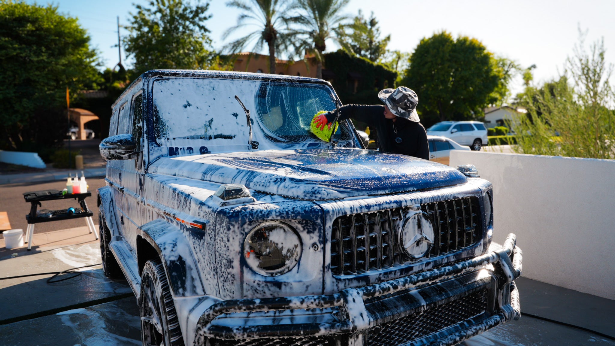 Pure Power Detailing contractor cleaning the windshield of a foam-covered blue Mercedes G-Wagon during a luxury hand wash at a residential property in Phoenix, Arizona
