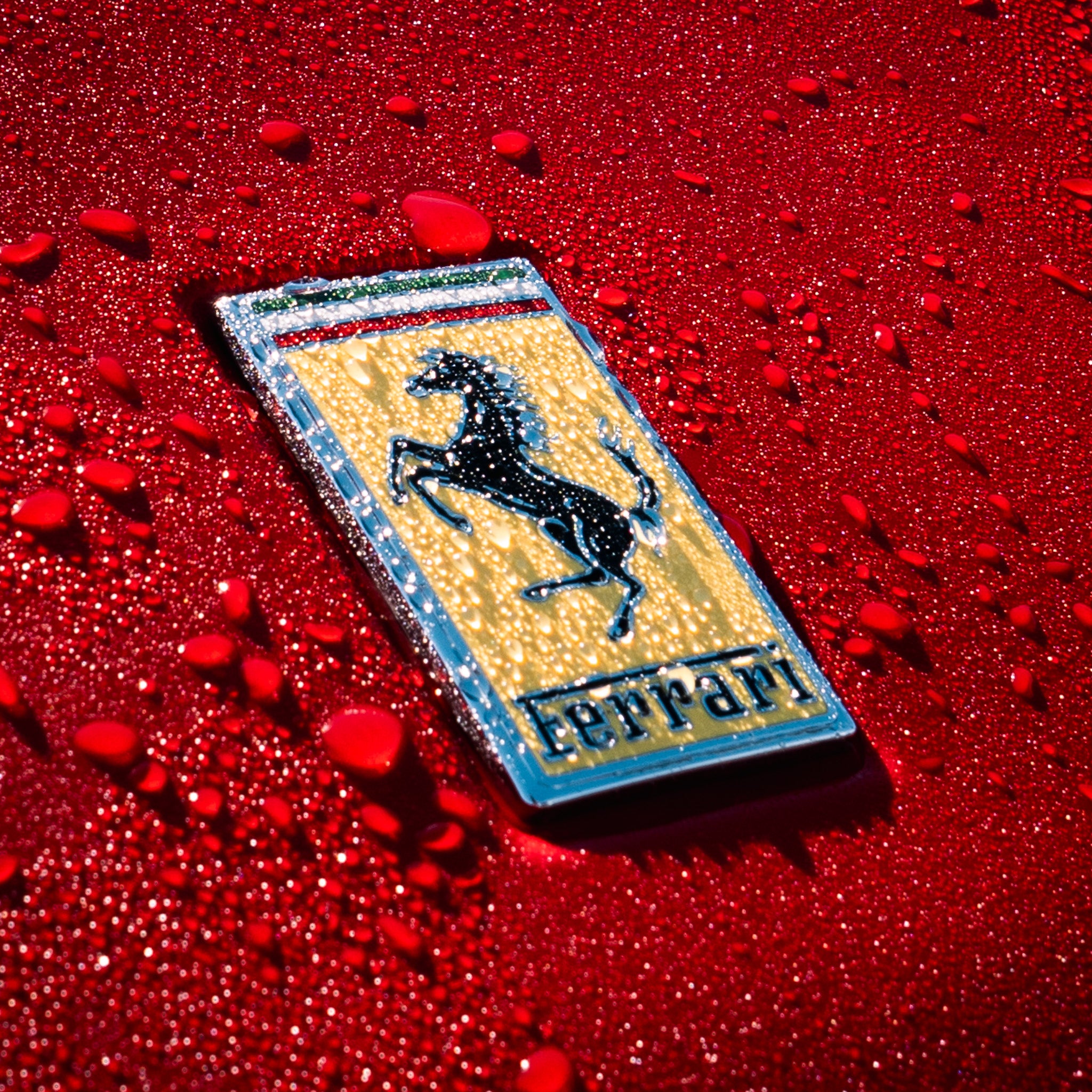 Close-up of a Ferrari emblem on a red hood covered in water beads during a professional detail by Pure Power in Phoenix, Arizona