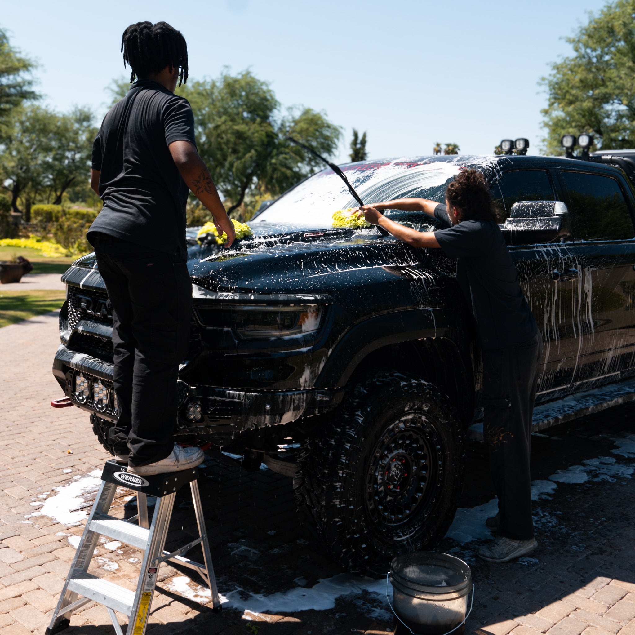 Two Pure Power Detailing contractors washing a lifted black TRX ram truck using foam, microfiber mitts, and a ladder during a mobile detailing service in Phoenix, Arizona