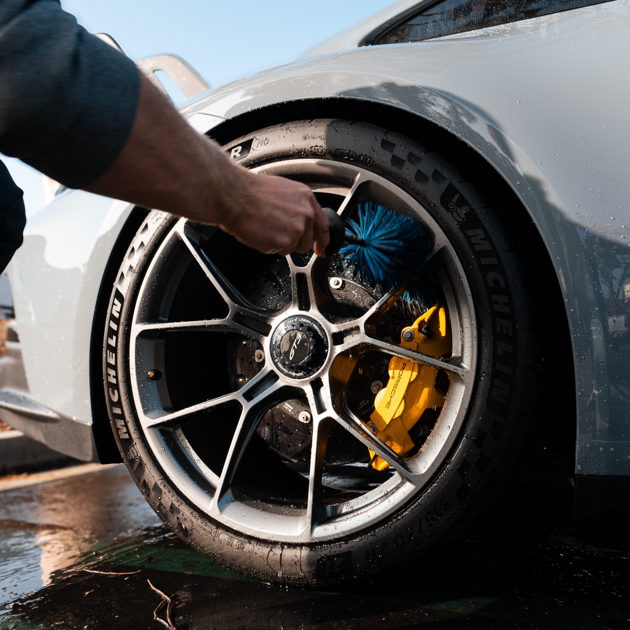 Close-up of a Pure Power Detailing contractor cleaning a Porsche wheel and yellow brake caliper using a soft detailing brush in Phoenix, Arizona